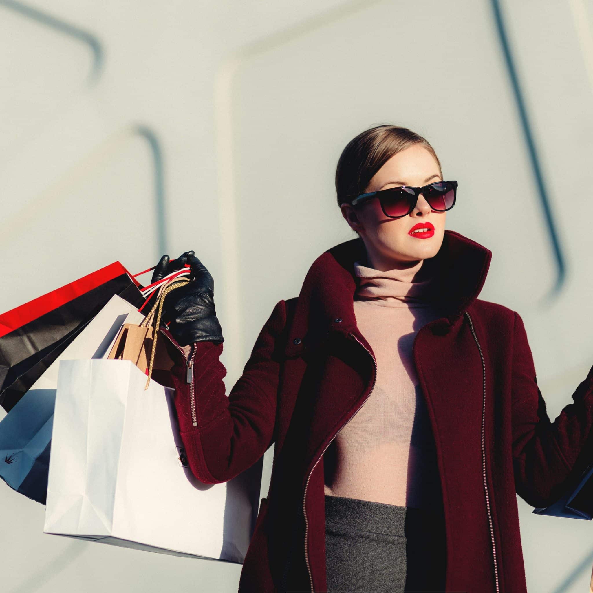 Jeune femme avec un manteau rouge, des lunettes de soleil et des sacs shopping